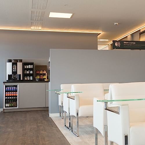 Modern airport lounge with white seating and refreshment area.
