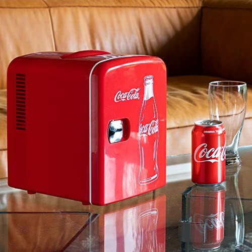 Red Coca-Cola mini fridge with a Coke can and glasses on a table.