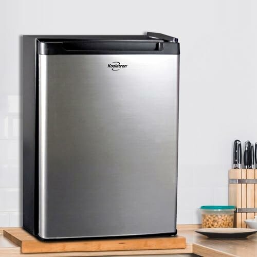 Compact stainless steel mini fridge on a wooden counter.